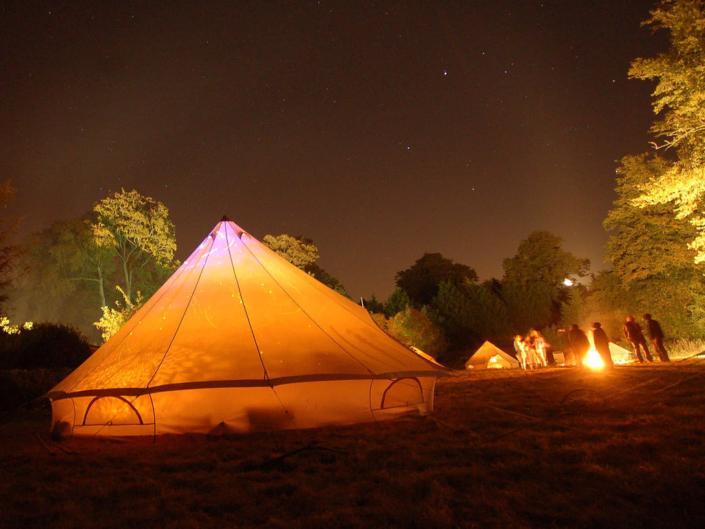 5m standard bell tent at night and people standing around a fire