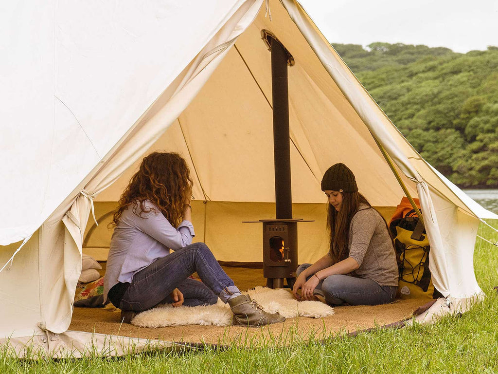 Two people sat next to a traveller stove inside a bell tent