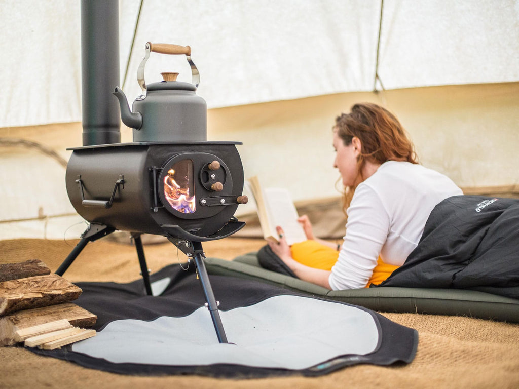 Woman reading next to a warm wood burning frontier plus bell tent stove