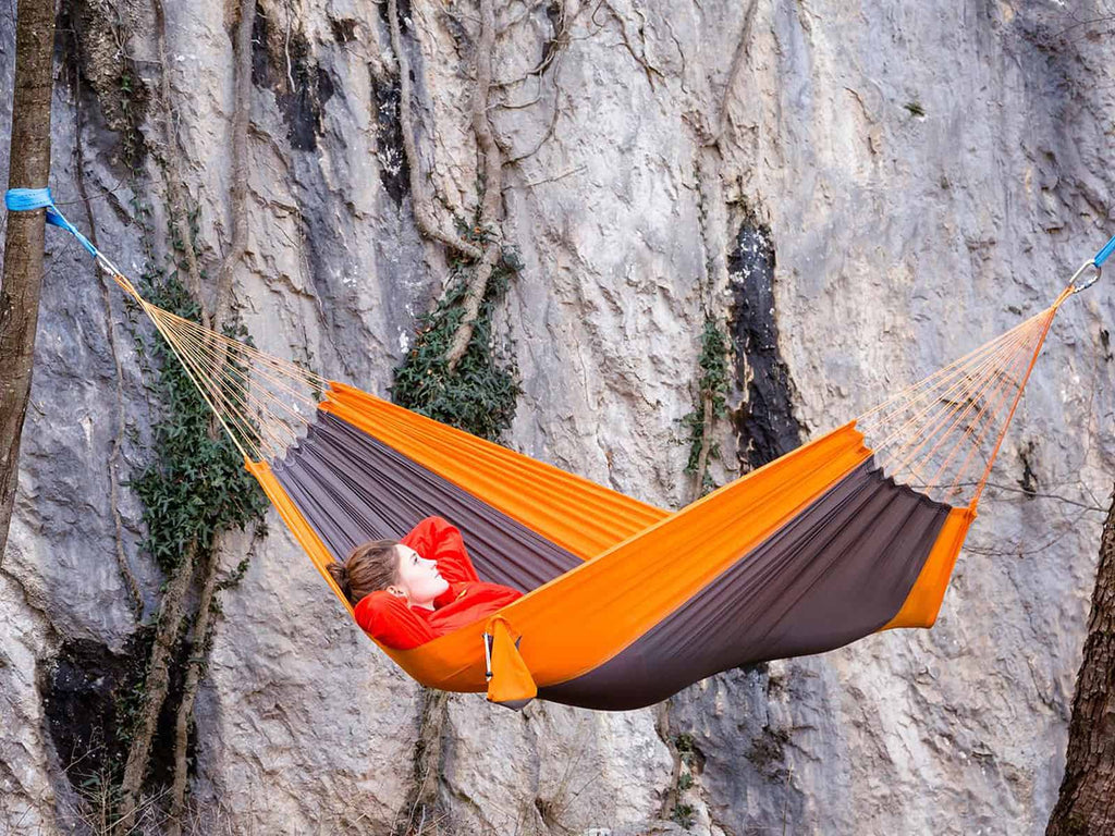 Woman in an orange parachute hammock between two trees