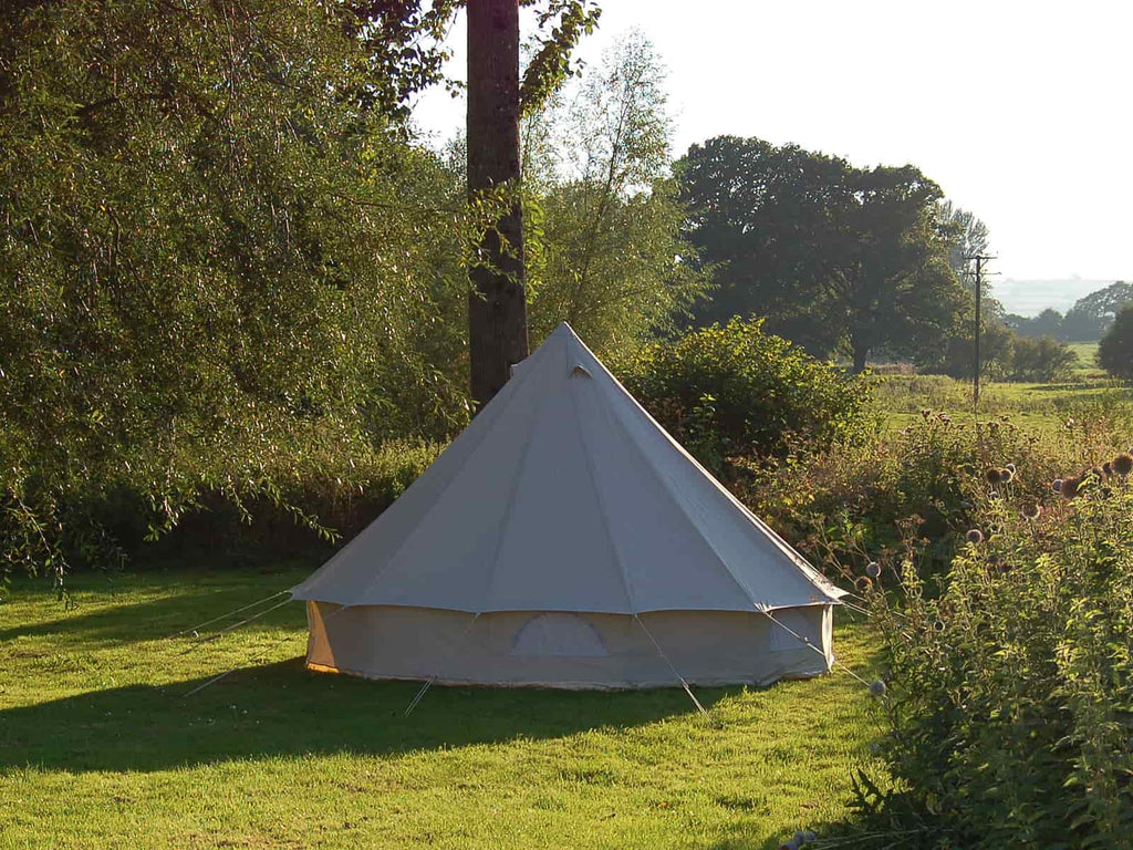 View of the back of a 4m standard bell tent pitched in the corner of a meadow