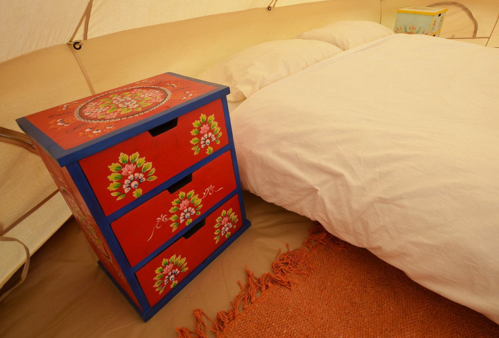 Red camping with soul chest of indian drawers and double bed inside a bell tent